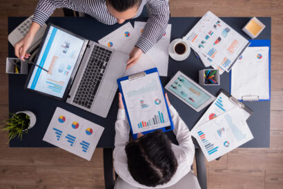 Top viewTop view of manager and employee doing teamwork in business office , looking at charts on laptop display. Finance paperwork with charts at workplace. Discusing financial plan.